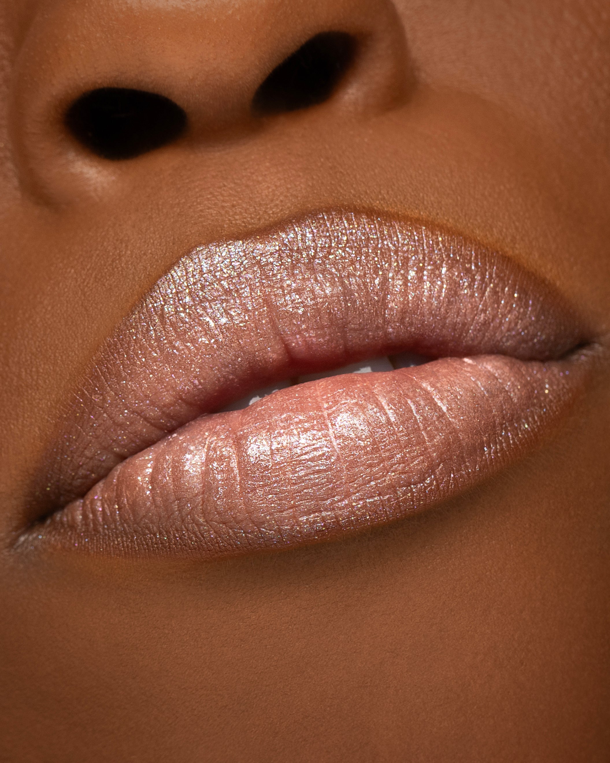 Close-up of a person's lips wearing a shimmery, metallic nude-pink lip gloss.